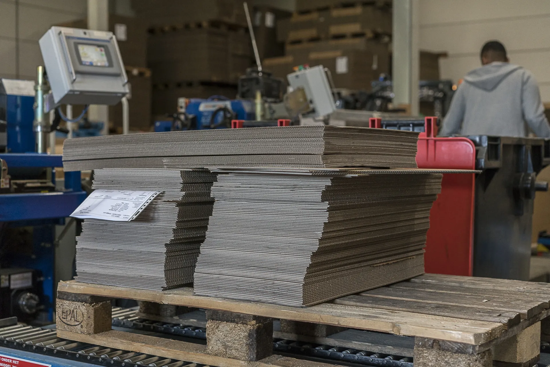 Gestapelte Kartonzuschnitte auf einer Palette in der Produktionshalle, bereit für die Weiterverarbeitung zu maßgefertigten Kartons. | Kartonsaufmass.de